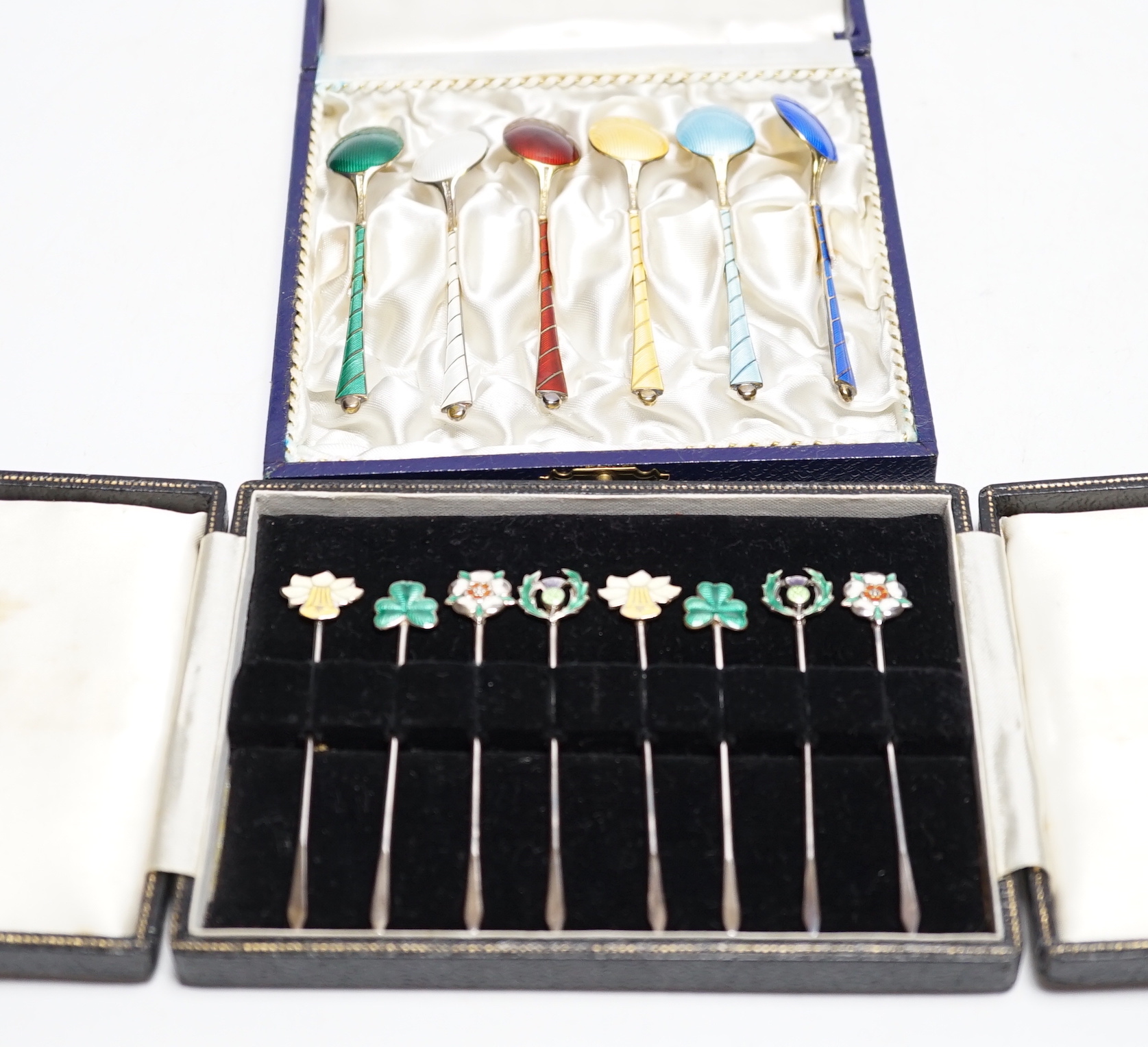 A cased set of six Danish gilt sterling and polychrome enamelled coffee spoons and a cased set of eight enamelled white metal cocktail sticks, stamped 'silver', the terminals decorated with the floral emblem of the count